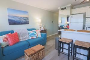 a living room with a blue couch and a kitchen at Charming Beachside Condo Lovely Pool Hot Tubs and Boardwalk in Galveston