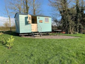 ein kleines blaues Haus mit einem Tisch auf einem Feld in der Unterkunft Delilah the shepherd's hut in Sidlesham