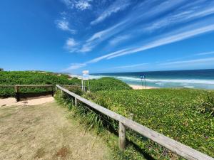 a wooden fence next to a beach with the ocean at The Entrance & Shelly Beach Holiday House in Long Jetty