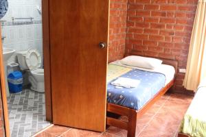 Cama pequeña en habitación con pared de ladrillo en Hostal Colibri 2, en Baños