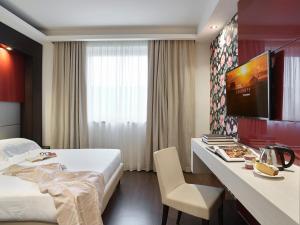 グラッソッビオにあるWinter Garden Hotel Bergamo Airportのベッド、デスク、テレビが備わるホテルルームです。