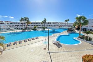 einen Blick über einen Pool mit Stühlen und Palmen in der Unterkunft Nice 2 bedroom flat with big Pools and big terrace Parque don José, 313 in Costa Del Silencio