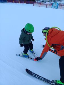 Un hombre está ayudando a un niño esquiando en la nieve en Śnieżnicki Domek - Masyw Śnieżnika, Sudety, en Stronie Śląskie