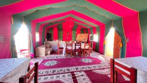 une salle à manger aux murs roses avec une table et des chaises dans l'établissement Sahara Luxury Camp, à Zagora