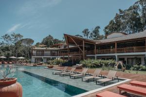 Un complejo con piscina con sillas y un edificio. en Aysú Trancoso Boutique Hotel, en Trancoso