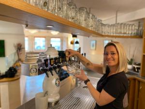 une femme se tient derrière un bar avec un verre dans l'établissement Vico's Hotel & Restaurant Asperg, à Asperg