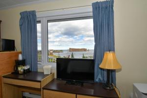 a room with a television and a window with blue curtains at Motel Nouvel Horizon in Perce