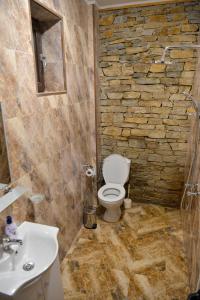 y baño con aseo, lavabo y pared de piedra. en Къщи за гости НЕСИ, en Leshten