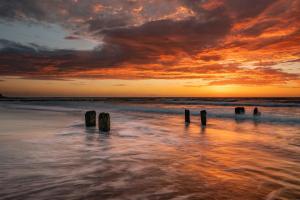 a sunset on a beach with wooden posts in the water at Park Design - Apartments M&M (Polanki Park) in Kołobrzeg