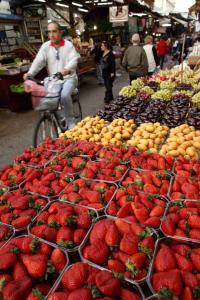 un hombre montando una bicicleta pasando una exposición de fresas en un mercado en Sun City Hotel en Tel Aviv