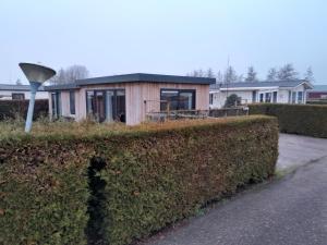 una casa pequeña es vista detrás de un seto en Luxe 5 persoons bungalow op rustig vakantiepark nabij Leeuwarden, en Dronrijp