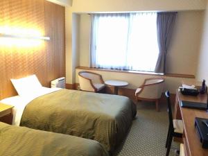 a hotel room with two beds and a desk and a window at Miyajima Coral Hotel in Miyajima
