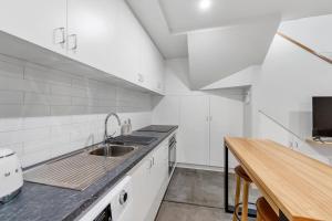 a white kitchen with a sink and a wooden table at Self Contained Loft Apartment in CBD in Devonport