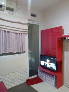 uma sala de estar com uma televisão e uma parede vermelha em Comfort 2BR green pramuka bougenvile em Jakarta