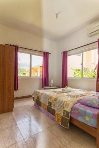 a bedroom with a bed with purple curtains and two windows at Josies Cottage in Beau Vallon