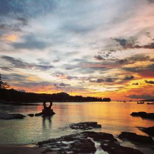 une personne assise sur un rocher dans l'eau au coucher du soleil dans l'établissement Gold Coast Phu Quoc Beach Resort, à Duong Dong