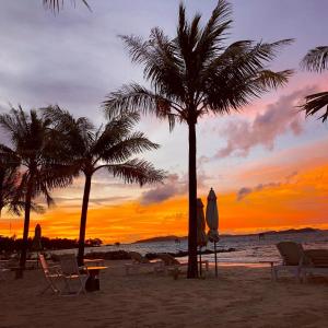 a sunset on a beach with palm trees and chairs at Gold Coast Phu Quoc Beach Resort in Phu Quoc