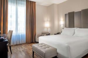 a hotel room with a large white bed and a chair at NH Collection Victoria in Granada
