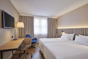 a hotel room with two beds and a desk at NH Frankfurt Airport in Kelsterbach