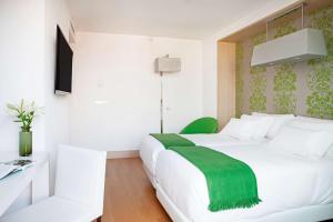 a bedroom with a white bed with a green blanket on it at NH Madrid Principe de Vergara in Madrid