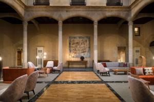 eine Lobby mit Stühlen, Tischen und einem Gemälde an der Wand in der Unterkunft NH Collection Salamanca Palacio de Castellanos in Salamanca