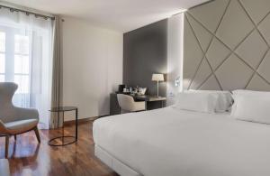 a bedroom with a large white bed and a chair at NH Collection Salamanca Palacio de Castellanos in Salamanca