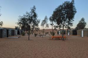 a picnic table and trees in the middle of a desert at Camel Trek Bivouac in Merzouga