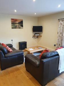 sala de estar con 2 sofás de cuero y TV en Shieling Cottage at Lovelady Shield, en Alston