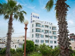 ein hohes weißes Gebäude mit Palmen und einem Straßenlicht in der Unterkunft Hotel Good Inn in Seogwipo