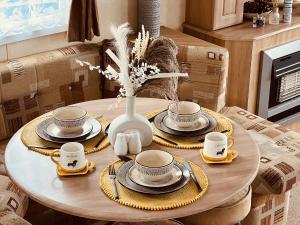 a table with plates and cups and a vase with flowers at Summer Dreams Holiday Home in Skegness