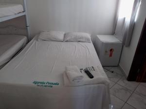 Una cama blanca con toallas y un mando a distancia. en Pousada Algaroba en Bom Jesus da Lapa