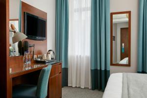 a hotel room with a desk with a television and a bed at Seraphine Hammersmith Hotel in London