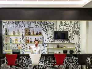 a man standing behind a counter in a room with red chairs at ibis Ankara Airport Hotel in Ankara