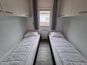 two beds in a small room with a window at Chalet 82 op Chaletpark Bregkoog in De Koog