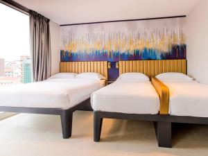 two beds in a room with a painting on the wall at ibis budget Singapore Gold in Singapore