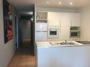 una cocina con armarios blancos, fregadero y electrodomésticos en Les Jasmins 8 pers Piscine commune calme et confort en Saint-Gilles