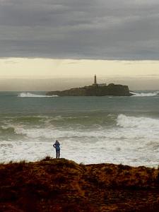 a person standing on a beach with a lighthouse in the ocean at Vistas al Mar in Somo