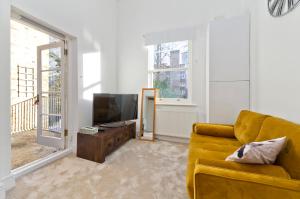 un soggiorno con divano giallo e TV di Bright one bedroom apartment with balcony in Maida Vale by UnderTheDoormat a Londra