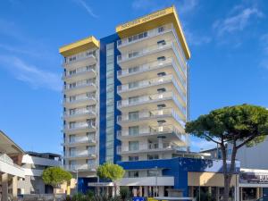 een hoog blauw-wit gebouw met een boom bij Nashira Apartments in Lignano Sabbiadoro