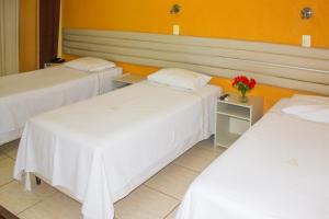 una habitación con 3 camas y un jarrón de flores sobre una mesa en Hotel Meri, en Conselheiro Lafaiete