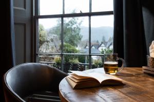 a glass of beer and a book on a table with a window at The Angel Inn - The Inn Collection Group in Bowness-on-Windermere