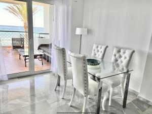 Sitio de CalahondaにあるMI CAPRICHO 172 Beachfront Apartmentのダイニングルーム(ガラステーブル、白い椅子付)