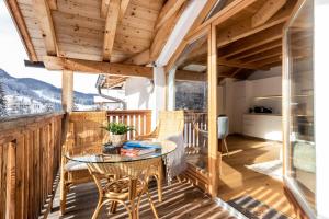 a wooden deck with a glass table and chairs at Casa Flora in Dobbiaco