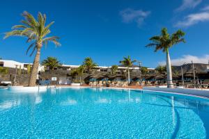 une grande piscine avec des palmiers et des bâtiments dans l'établissement Dreamplace Bocayna Village, à Playa Blanca