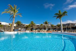 een groot zwembad met palmbomen en gebouwen bij Dreamplace Bocayna Village in Playa Blanca