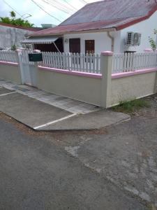 a white house with a pink fence and a parking lot at Maison créole chaleureuse avec stationnement in Le Gosier