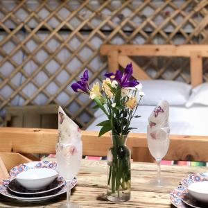 a table with a vase of flowers and two glasses at 'Villager' the Yurt at Pentref Luxury Camping in Penuwch +14 photos