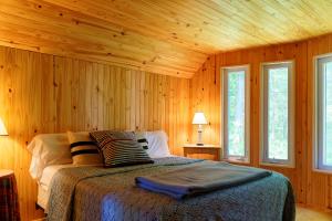 a bedroom with a bed with wooden walls and windows at Black River Cottage in Milford