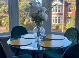 a glass table with a vase of flowers and green chairs at Hidden Gem w/ parking Short walk to Pleasure Beach in Blackpool