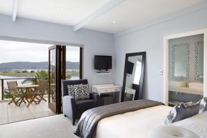 a bedroom with a bed and a balcony with a television at Tides End Manor House in Knysna